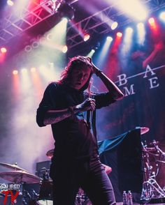 a man with long hair standing on stage in front of some microphones and lights