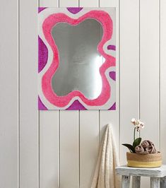 a mirror on the wall next to a small table and stool with a potted plant