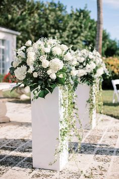 two white vases filled with flowers on top of a stone walkway