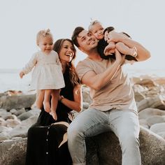 a man, woman and child are sitting on rocks by the ocean with their arms around each other