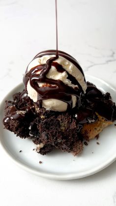 a white plate topped with a chocolate dessert covered in ice cream and drizzle