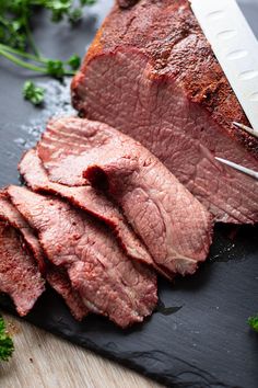 sliced meat sitting on top of a black cutting board next to broccoli and a knife