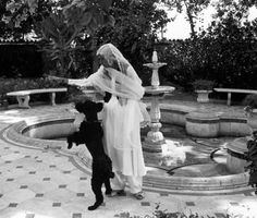 a woman in a wedding dress standing next to a black dog on a tiled floor