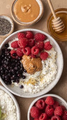 three bowls filled with different types of food next to some honey and raspberries