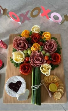 an arrangement of flowers on a cutting board with crackers and cookies next to it