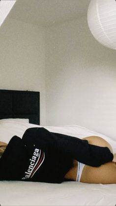 a woman laying on top of a bed next to a white lamp and black headboard