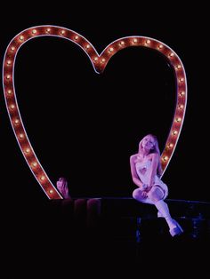 a woman sitting on top of a bench in front of a heart shaped light up sign