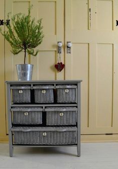 a gray dresser with baskets and a potted plant