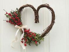 a heart shaped wreath with red berries and greenery hangs on a white painted door