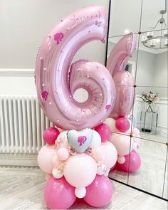 the number six balloon is pink and has hearts on it, while balloons are arranged around it