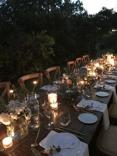 a long table is set with candles and place settings for an outdoor dinner party in the evening