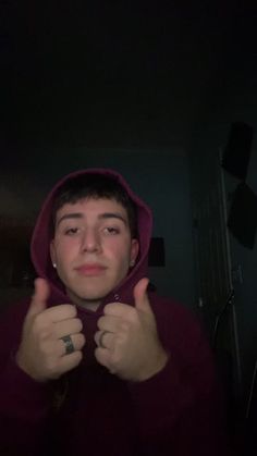 a young man in a red hoodie is holding his thumb up to the camera