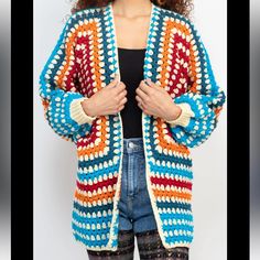 a woman standing in front of a white wall wearing a colorful crochet cardigan