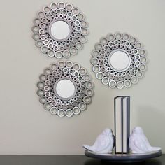 three circular mirrors on the wall above a book and two white bird figurines