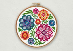 a cross stitch pattern with colorful flowers in the center on a white wall hanging from a wooden frame