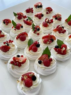 a white plate topped with mini desserts covered in whipped cream and berries