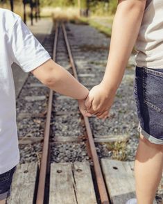 two children holding hands while standing on train tracks