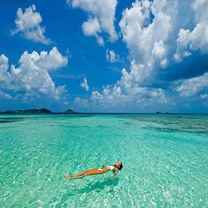 a woman floating in the ocean on top of a body of water with an island in the background