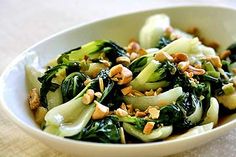 a white bowl filled with vegetables and nuts on top of a beige cloth covered table