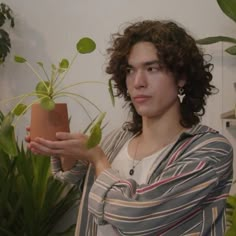 a woman holding up a potted plant in her right hand and looking at the camera