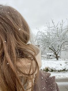 a woman standing in the snow with her back to the camera, holding a cell phone up to her ear