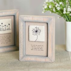 two framed pictures with dandelions in them on a table