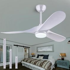 a white ceiling fan in a bedroom next to a bed with pillows and blankets on it