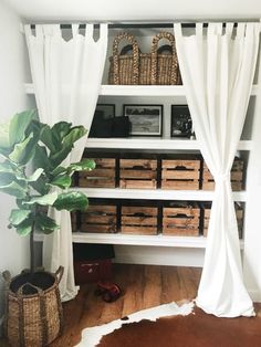 a living room with white curtains and baskets on the shelves next to a potted plant