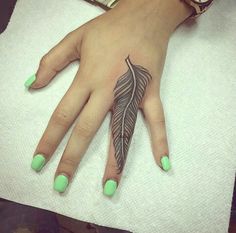 a woman's hand with green nails and a black feather tattoo