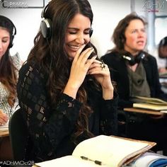 a woman wearing headphones while talking on her cell phone in front of other people