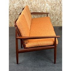 an orange couch sitting in front of a wall with a wooden frame and armrests