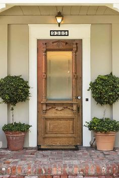 two potted plants are on either side of the front door, and one planter is next to it