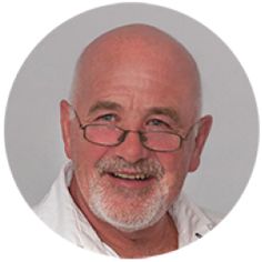 an older man with glasses and a white beard smiles in a round photo, while looking at the camera