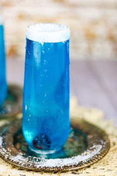 two blue drinks sitting on top of a table next to each other in front of a plate