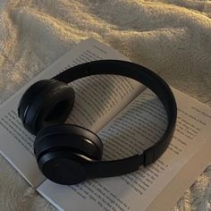 an open book with headphones on top of it sitting on a bed next to a pair of headphones