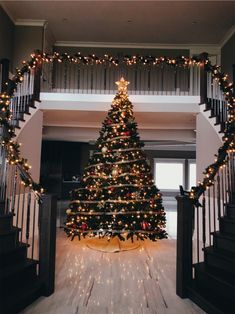 a decorated christmas tree sitting in the middle of a living room next to a stair case