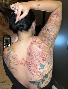 a woman with tattoos on her back is combing her hair