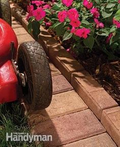 a red lawn mower sitting on top of a brick walkway next to pink flowers