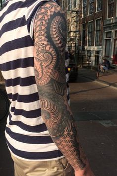 a man with a tattoo on his arm standing in front of a building and looking down at the street