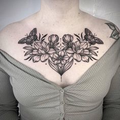 a woman's chest with flowers and butterflies on her upper back shoulder, which is covered in black ink