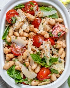 a white bowl filled with pasta salad topped with tomatoes and spinach leafy greens