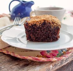 a close up of a piece of cake on a plate with a cup of coffee