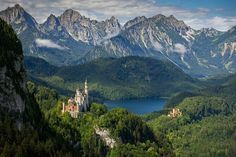 an aerial view of a castle in the middle of a forest with mountains behind it