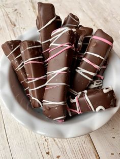 a white bowl filled with chocolate covered candy sticks on top of a wooden table next to a cup of coffee