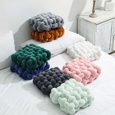 four different colored pillows sitting on top of a white bed next to a night stand