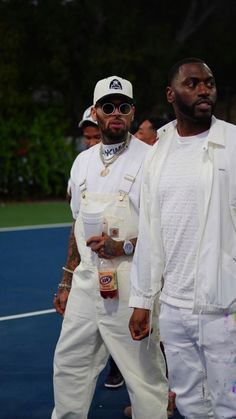 two men standing next to each other on a tennis court with people in the background