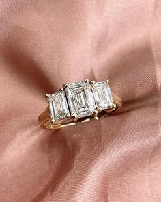 three stone diamond ring sitting on top of a pink satin surface with gold trimming