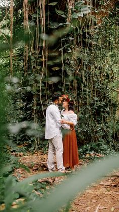 a man and woman standing next to each other in front of a tree covered with vines