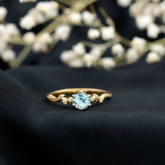 a gold ring with an aqua blue topazte surrounded by white flowers on a black cloth