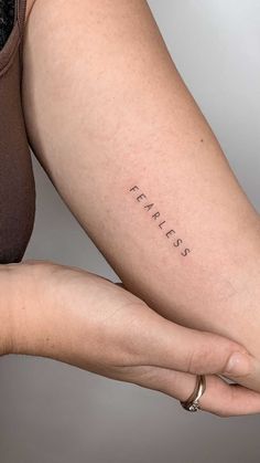 a woman's arm with the word fearless tattooed on her left side, in black ink